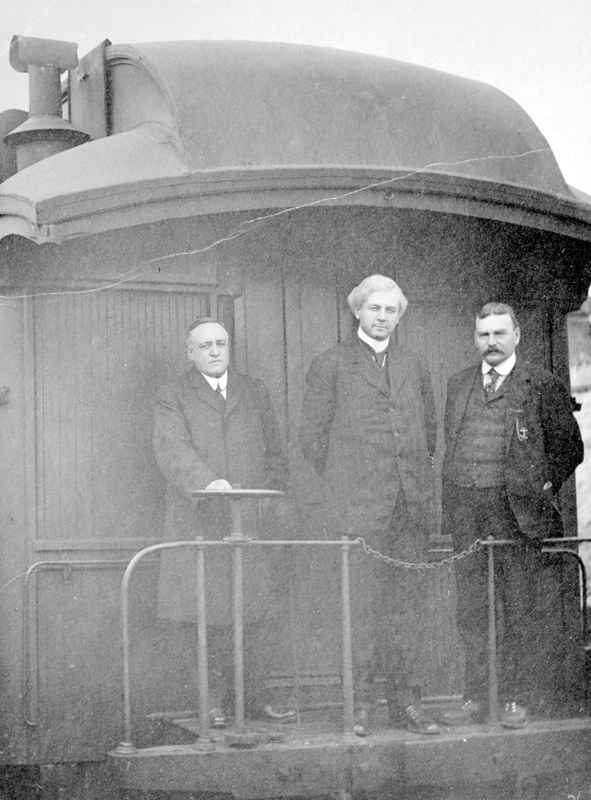 Richard McBride (Premier from 1903 to 1912), William John Bowser (Premier from 1915 to 1916), and business-owner Tom Abriel pose on a train during the 1912 provincial election. McBride and Bowser ran as members of the B.C. Conservative Party.