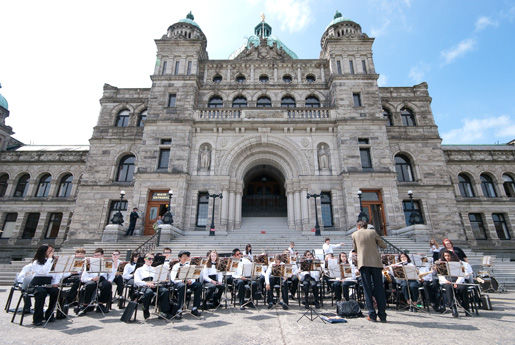 A school band with about 40 students are seated in front of the building looking at their conductor